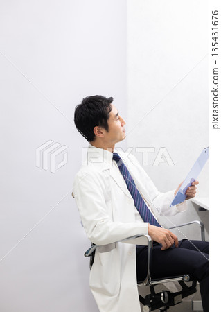 一位身穿白大褂的男醫生抬起頭,手裡拿著一份病歷。 一位身穿白大褂的男醫生抬起頭,手裡拿著一份病歷。 135431676