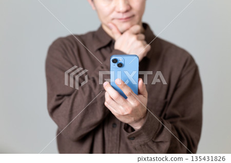 一位中年男子看著他的智慧型手機，憂心忡忡。 135431826