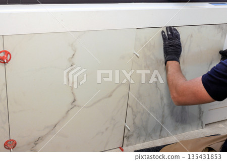 Worker installs large tiles on wall in kitchen during home renovation project 135431853