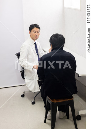 A male doctor in a white coat examining a male patient A male doctor in a white coat examining a male patient 135431871