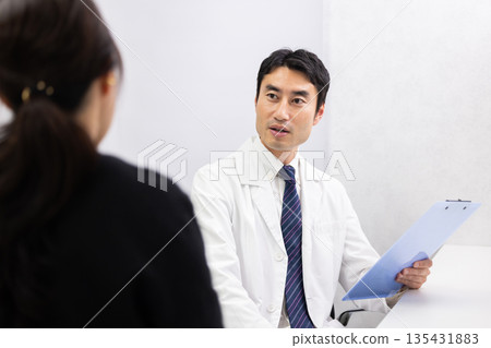一位身穿白大褂的男醫生正在檢查一位女病人。 一位身穿白大褂的男醫生正在檢查一位女病人。 135431883