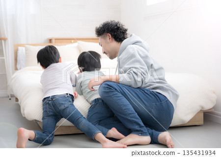 Family time on a holiday with a father and two children relaxing in bed. Full-body view of the back of a man in denim without a face. Family time on a holiday with a father and two children relaxing in bed. Full-body view of the back of a man in denim without a face. 135431934
