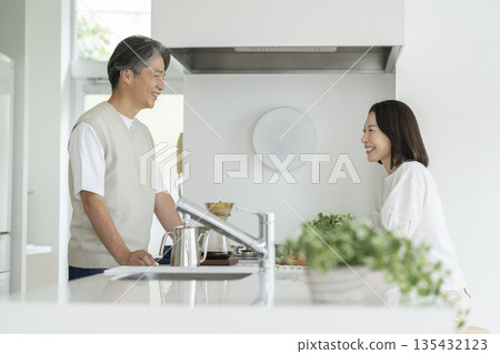 一對五十多歲、面帶笑容的夫婦隔著廚房櫃檯聊天。 135432123