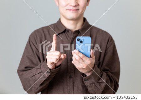 A middle-aged man holding a smartphone and pointing his index finger A middle-aged man holding a smartphone and pointing his index finger 135432155