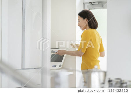 A woman in her 50s warming up her lunch in the microwave 135432210