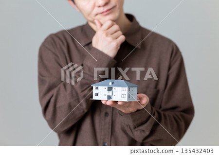 A middle-aged man holding a model of an apartment building and worrying 135432403