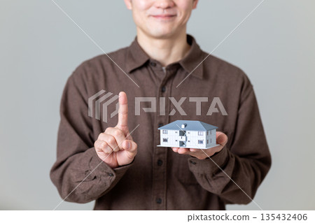 一位中年男子手持公寓大樓模型，食指向上指著。 135432406