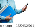 Close-up of Asian businessman holding blue folders in one hand and using smartphone with the other, representing multitasking, office work, document management, and digital communication efficiency 135432501