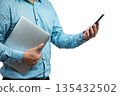 Close-up of Asian man in striped shirt holding a laptop and using smartphone, representing modern business communication, remote work, digital productivity, and multitasking in professional lifestyle 135432502