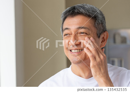 Senior man smiling and holding his hand on his cheek Senior man smiling and holding his hand on his cheek 135432535