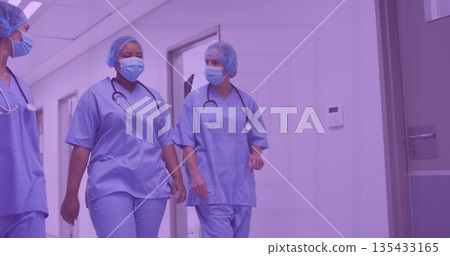 Walking three staff in hospital corridor wearing blue scrubs face masks hair nets with stethoscopes 135433165