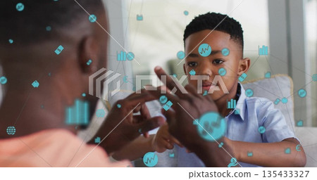 Father and son playing counting game on sofa in living room, with blue digital finance icons Father and son playing counting game on sofa in living room, with blue digital finance icons 135433327
