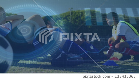 Kneeling female soccer player tying cleat in bib on soccer field, with soccer ball and cones Kneeling female soccer player tying cleat in bib on soccer field, with soccer ball and cones 135433365