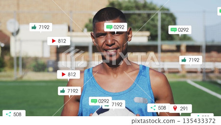 Standing male in blue sleeveless top holding soccer ball on soccer field, with social media icons Standing male in blue sleeveless top holding soccer ball on soccer field, with social media icons 135433372