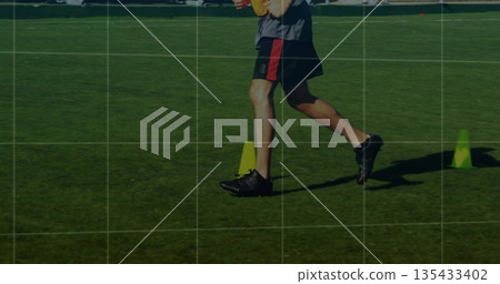 Legs wearing sportswear performing agility drill in sunlit grass field, with training cones 135433402