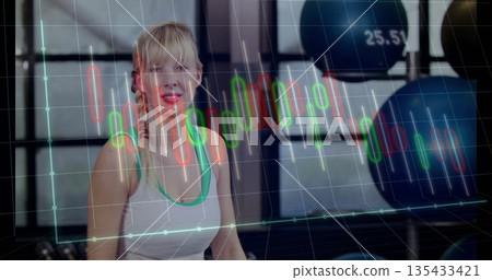 Smiling blonde woman wearing sportswear in fitness studio, with medicine balls and chart overlay 135433421