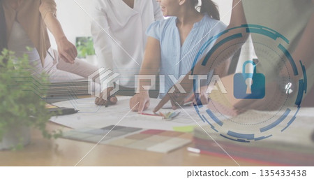 Leaning designers wearing blouses reviewing blueprints in office, with color swatches, lock icon Leaning designers wearing blouses reviewing blueprints in office, with color swatches, lock icon 135433438