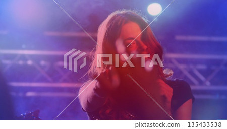 Singing woman holding microphone and extending hand at concert stage with metal truss, colored haze Singing woman holding microphone and extending hand at concert stage with metal truss, colored haze 135433538