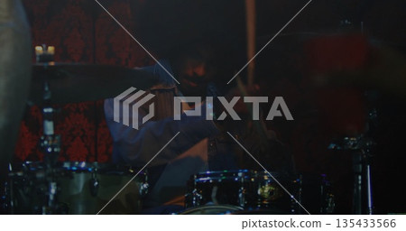 Playing Indian drummer hitting drums and cymbals on club stage, with denim jacket and drumsticks 135433566