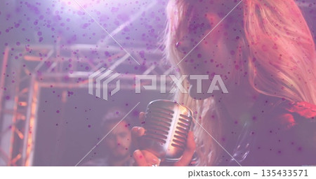 Singing female vocalist holding vintage microphone on dim stage, with electric guitar and truss Singing female vocalist holding vintage microphone on dim stage, with electric guitar and truss 135433571