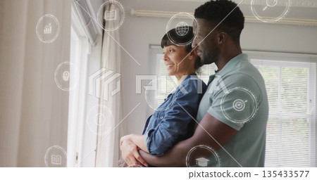 Embracing couple standing by large window at home, with horizontal blinds and curtains 135433577