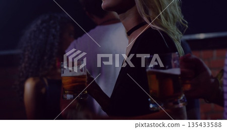 Chatting friends wearing choker necklace holding glass beer mugs at bar at night against brick wall Chatting friends wearing choker necklace holding glass beer mugs at bar at night against brick wall 135433588