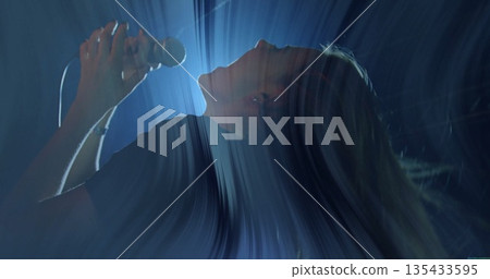 Leaning female vocalist in dark shirt singing on stage under blue-white beams with wired microphone Leaning female vocalist in dark shirt singing on stage under blue-white beams with wired microphone 135433595