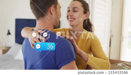 Smiling woman embracing man in modern bedroom, with blue chat bubble showing 36 messages Smiling woman embracing man in modern bedroom, with blue chat bubble showing 36 messages 135433596