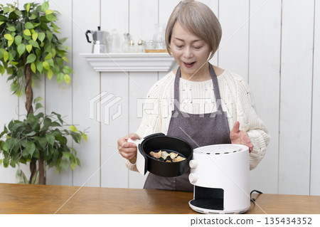Senior woman making snack potato chips in an air fryer Senior woman making snack potato chips in an air fryer 135434352