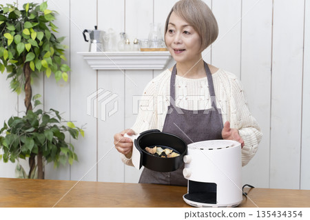 Senior woman making snack potato chips in an air fryer Senior woman making snack potato chips in an air fryer 135434354