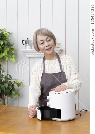 Senior woman making snack potato chips in an air fryer Senior woman making snack potato chips in an air fryer 135434356