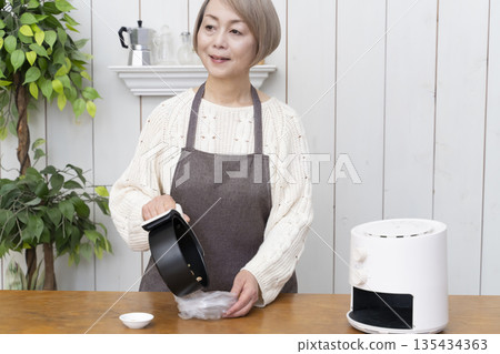 Senior woman making snack potato chips in an air fryer Senior woman making snack potato chips in an air fryer 135434363
