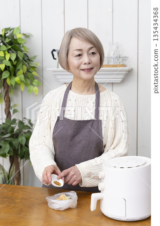 一位老年婦女用氣炸鍋製作薯片零食 一位老年婦女用氣炸鍋製作薯片零食 135434368