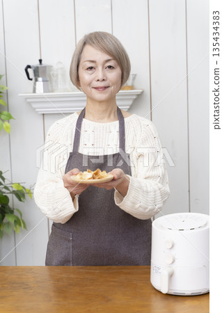 Senior woman making snack potato chips in an air fryer Senior woman making snack potato chips in an air fryer 135434383