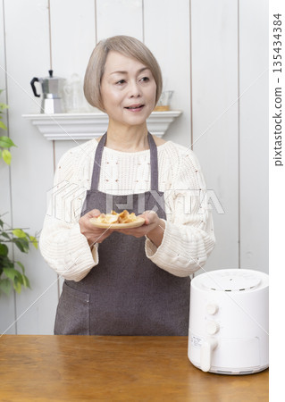一位老年婦女用氣炸鍋製作薯片零食 135434384