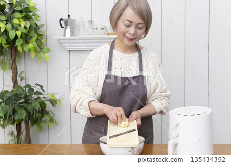 Senior woman making snack potato chips in an air fryer Senior woman making snack potato chips in an air fryer 135434392