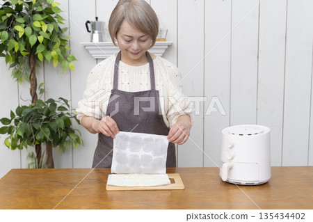 Senior woman making snack potato chips in an air fryer Senior woman making snack potato chips in an air fryer 135434402