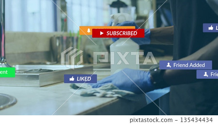 Gloved man wiping steel countertop in kitchen with spray bottle, rag and social icons, copy space 135434434