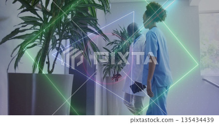 Walking nurse in scrubs and physician to elevator in hospital hallway with tablet under neon shapes 135434439
