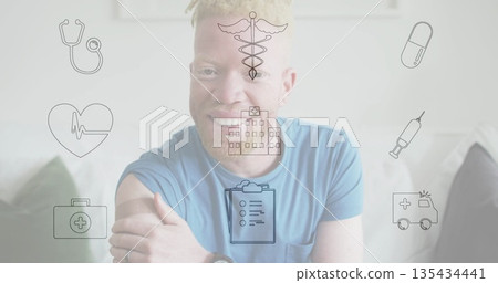 Smiling man in t shirt with wristwatch touching arm on sofa at home, floating medical icons 135434441