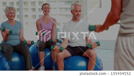 Performing arm curls participants sitting on blue stability balls in studio, with green dumbbells Performing arm curls participants sitting on blue stability balls in studio, with green dumbbells 135434552