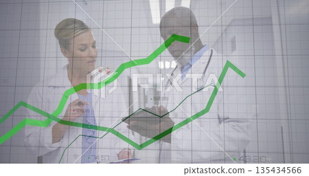 Standing doctors with clipboard and tablet reviewing data in hospital corridor, with graph overlay 135434566