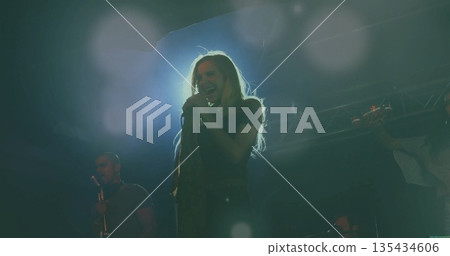 Female lead singer holding microphone and performing on stage, with mic stand, guitar, lights 135434606