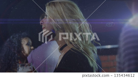 Blonde woman wearing black top and choker holding glass of beer at bar, with lens flare 135434612