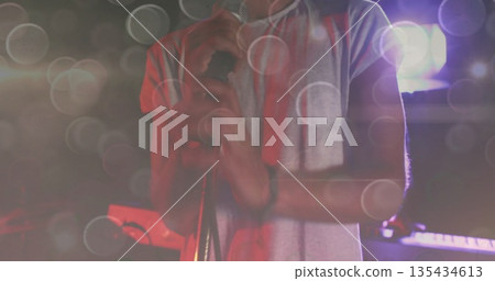 Gripping mic stand male singer performing on dark stage under spotlights, with towel and keyboard 135434613