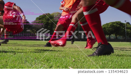 Sprinting soccer players wearing red uniforms, cleats on field at park with orange bib code overlay 135434623