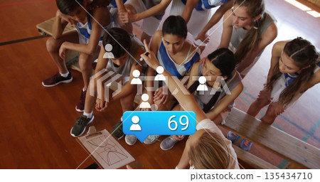 Pointing coach in polo instructing basketball players in jerseys at school gym, with clipboard Pointing coach in polo instructing basketball players in jerseys at school gym, with clipboard 135434710