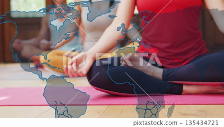 Practicing yoga group sitting with legs crossed in studio wearing tank tops leggings over world map Practicing yoga group sitting with legs crossed in studio wearing tank tops leggings over world map 135434721