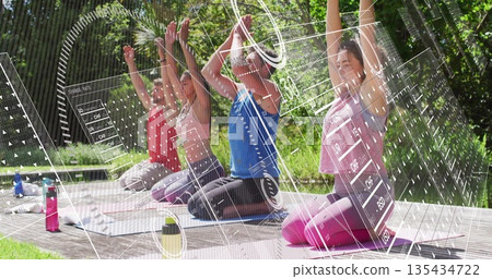 Stretching yoga group in fitness gear raising arms on platform in park, with mats, water bottles 135434722
