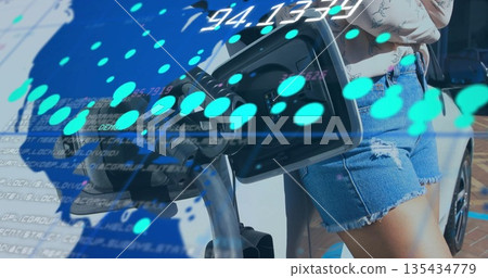 Woman wearing denim shorts inserting black connector into EV at parking bay, with teal data overlay 135434779